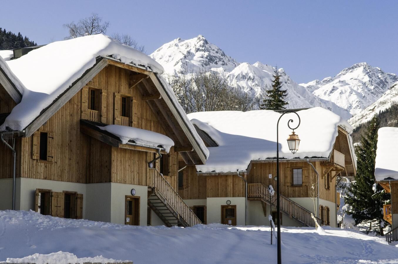 Un chalet en bois avec un escalier menant à un balcon, entouré de montagnes enneigées.