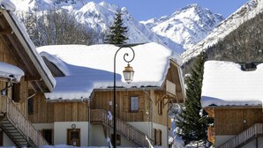 Una cabaña de madera con una escalera que lleva a un balcón, rodeada de montañas nevadas.