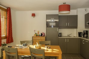 Una cocina compacta con comedor, que incluye una mesa de madera, sillas, un microondas, un lavamanos y una lámpara colgante roja.