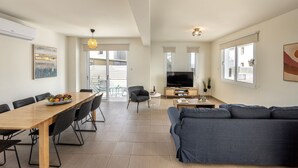 Uma sala de estar ampla com uma mesa de jantar, sofá, TV e grandes janelas.