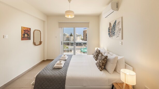 Quarto com cama, luminária de cabeceira, janela com vista e porta para uma varanda.