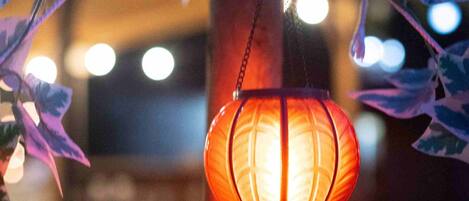 Um candeeiro suspenso com luz quente, rodeado por folhas decorativas e uma estrutura de madeira.