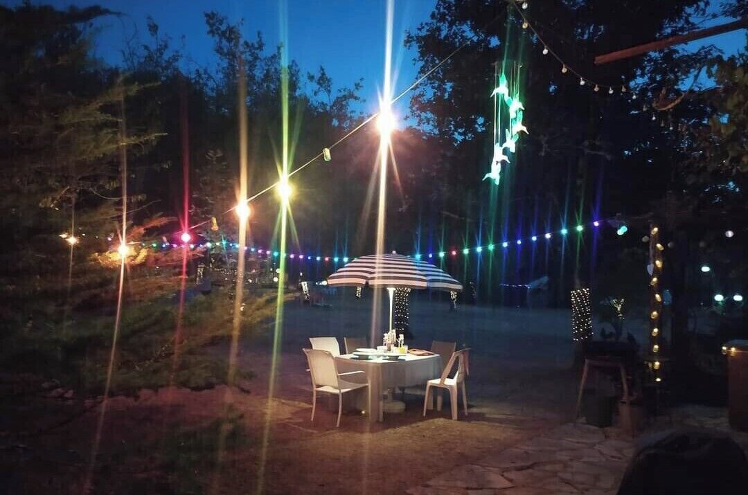 Een terras met een tafel, stoelen, lichtjes en een gestreepte parasol.