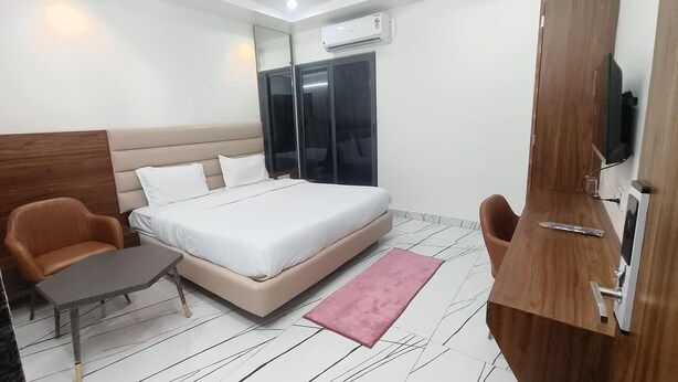 Una habitación de hotel moderna con una cama, dos sillones, una mesita, un espejo y un televisor.