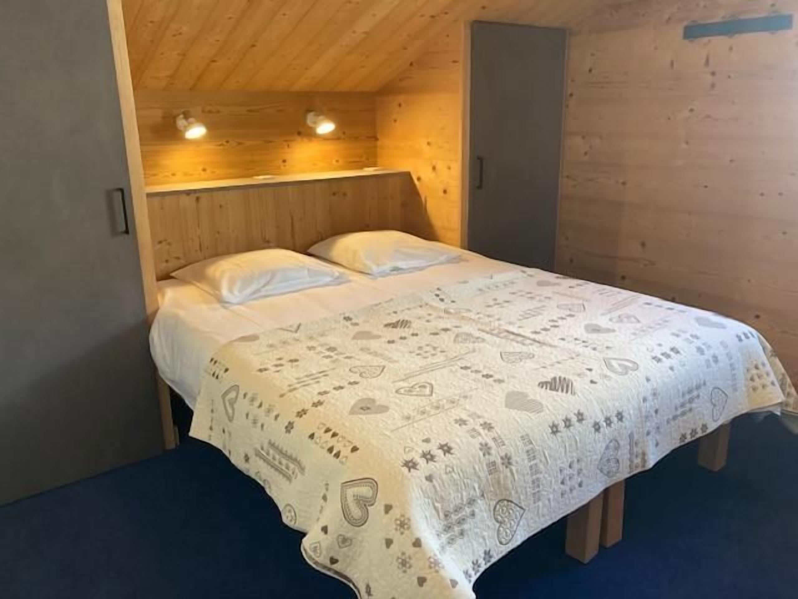 Una habitación tipo cabaña de madera con una cama, dos lámparas de noche y un cabecero de madera.