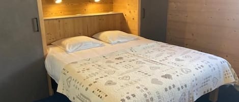Una habitación tipo cabaña de madera con una cama, dos lámparas de noche y un cabecero de madera.