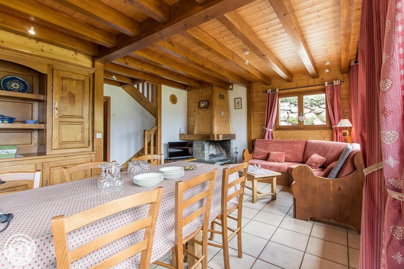 A cozy cabin interior with a dining area, wooden furniture, a fireplace, and a sofa.