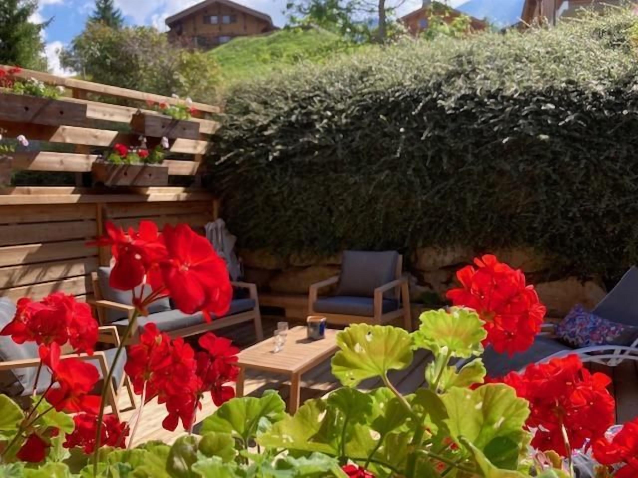 A wooden deck with outdoor furniture and vibrant red flowers.