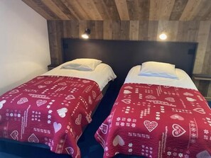 Duas camas de casal com roupa de cama vermelha estampada com corações, dispostas sob um teto de madeira com iluminação embutida.