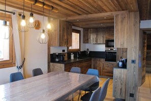 Eine moderne Küche mit Holzausstattung, einem Esstisch und Pendelleuchten.