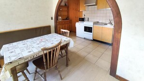 Un área de comedor con una mesa cubierta por un mantel, sillas de madera y un arco que da a una cocina con estufa, microondas y armarios de madera.
