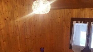 Habitación con paneles de madera, una cama, una mesita de noche, una lámpara y un ventanal con cortinas.