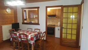 Un comedor con una mesa dispuesta para cuatro personas, un televisor y una pared de madera con un reloj.