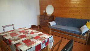 Una habitación acogedora con suelo de madera, un sofá azul con cojines estampados, un aparador de madera y una mesa con colcha.