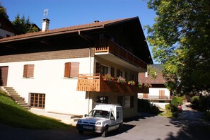 A two-story building with a balcony, a parked car, and a staircase leading to the entrance.