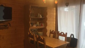 Un comedor de madera con una mesa y sillas, un estante con cristalería, y un televisor montado en la pared.