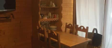 Puisesta materiaalista valmistettu ruokailutila, jossa on pöytä ja tuolit, hylly lasiesineille ja seinälle asennettu televisio.