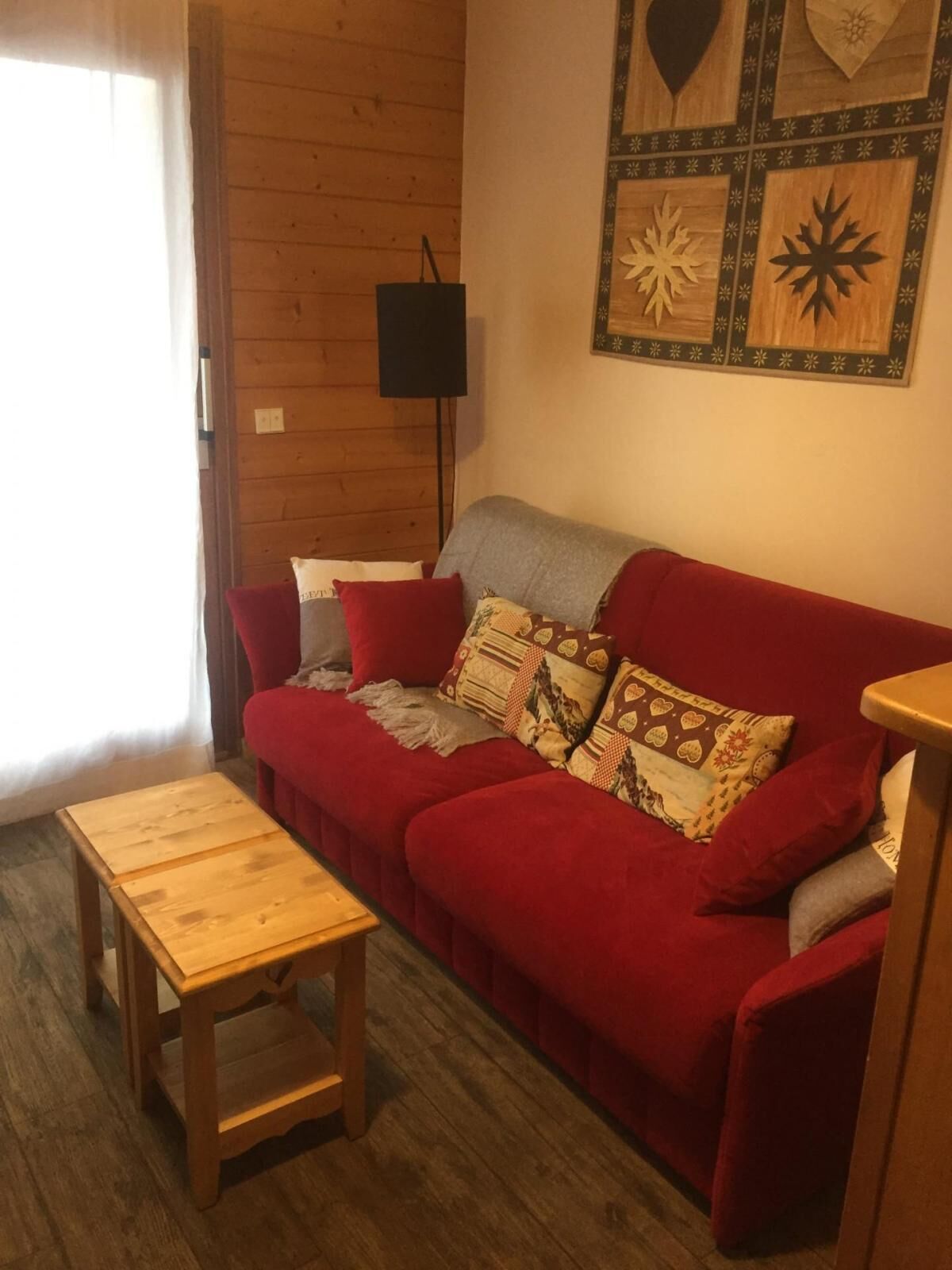 A cozy living room with a red sofa, a wooden coffee table, and a wall decorated with geometric patterns.