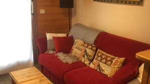 Una sala de estar acogedora con un sofá rojo, una mesa de centro de madera y una pared decorada con patrones geométricos.