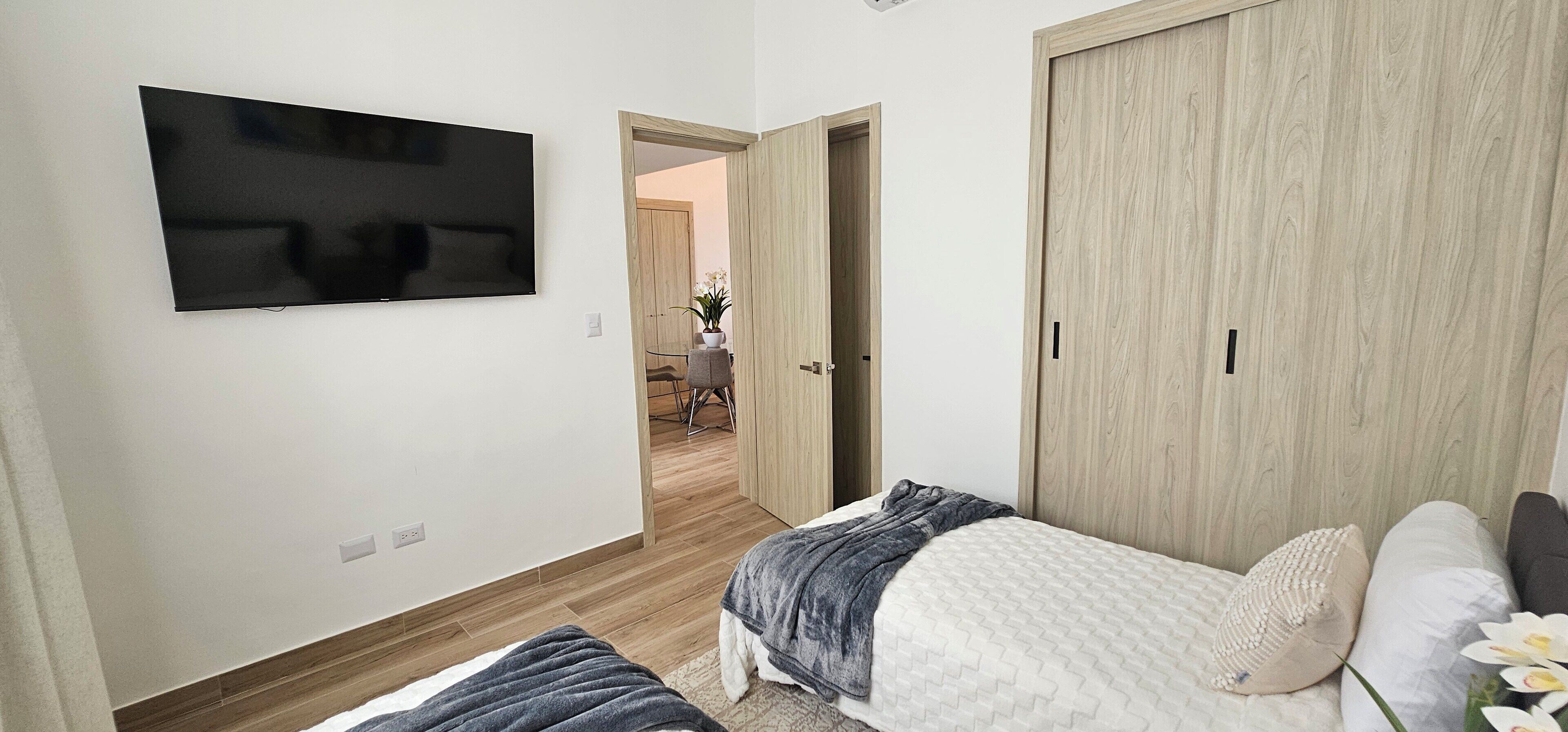 Un dormitorio con una cama, un televisor montado en la pared y un armario de madera.