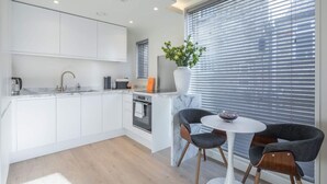 Een moderne keuken met witte kasten, een ingebouwde oven en een eethoek met een ronde tafel en twee stoelen.