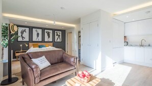 Een modern appartement met een slaapkamer, een zithoek met een bruine leren bank, een keuken en een eethoek.