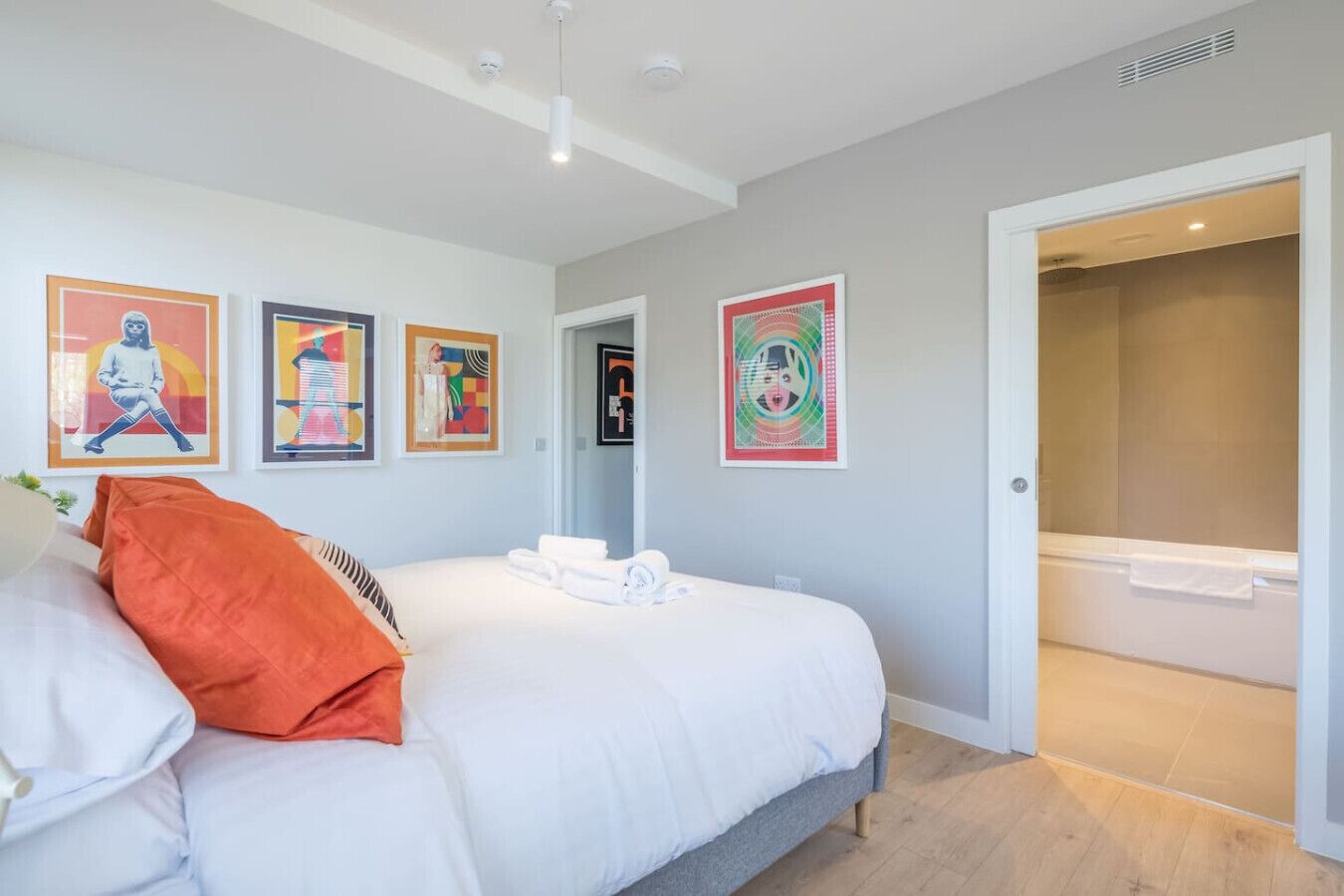 Een slaapkamer met een bed, een badkamer met een badkuip en vier kunstwerken in lijsten aan de muur.