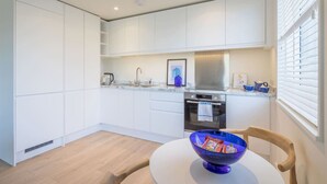 Una cucina moderna con mobili bianchi, un forno in acciaio inossidabile e un'area pranzo con un tavolo rotondo e una ciotola blu.