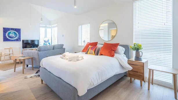 Una camera da letto moderna con un letto grande, un divano grigio, una TV e un'area pranzo.