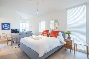 A modern bedroom with a large bed, a grey sofa, a TV, and a dining area. - Luxury Central Apt - Riverside Views & Parking! (Cambridge)
