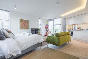 Une chambre d’hôtel moderne avec un grand lit, un canapé vert, une télévision et un coin cuisine.
