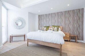 A modern bedroom with a large bed, a bedside table, a bench, a mirror, and a wooden slatted wall.
