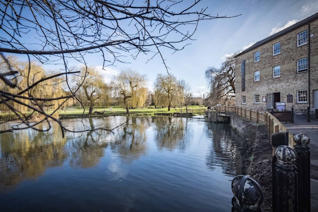 A calm river with a bridge, trees, and a building with a sign that reads "The Old Mill."