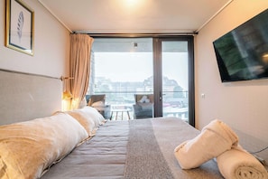 A hotel room with a bed, a TV, a balcony with a view, and a table with chairs. - HOM I 1D1B, Calefaccion Central, Piscina temperada, WiFi, Estacionamiento (Puerto Varas)