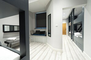 Un dormitorio moderno con cama, ventana, un banco con cojines y un armario empotrado.