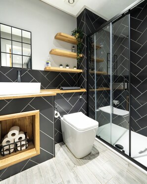 Un baño moderno con salpicadero de azulejos blanco y negro, tocador de madera, inodoro y cabina de ducha de vidrio.