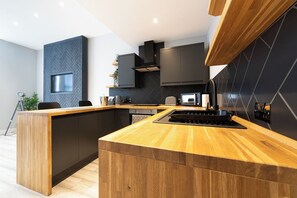 Una cocina moderna con una isla de madera, muebles negros y un salpicadero con estampado de espiga.