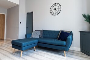 Un salon moderne avec un canapé d’angle bleu, une horloge murale et une porte.
