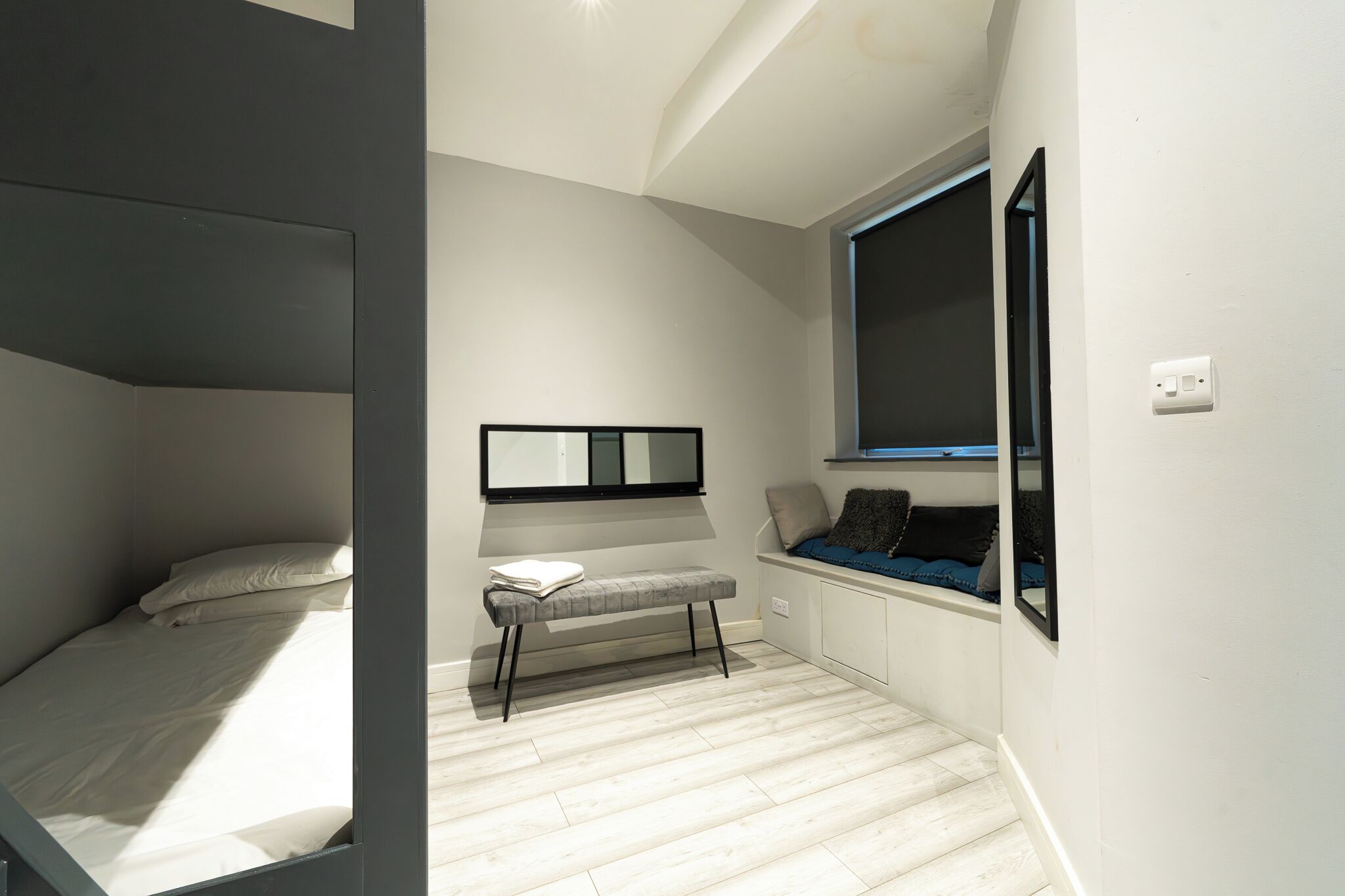 Un dormitorio con una cama litera, un pequeño banco, un espejo y una ventana con vistas.