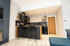 A compact kitchen with a wooden countertop, two black bar stools, and a built-in dishwasher.