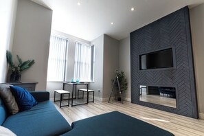 Una sala de estar moderna con un sofá, una mesita, un televisor montado en una pared con motivo de espiga y una planta en maceta.