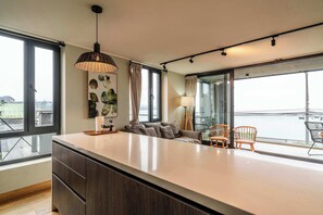 Una cocina moderna con una isla grande, un comedor con sillas, un sofá y vista al agua.