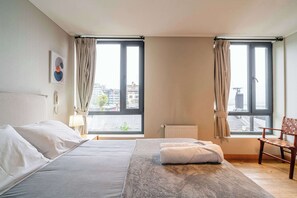 Une chambre d’hôtel avec un lit, deux fenêtres, un radiateur, une chaise et une lampe.