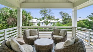A covered outdoor seating area with wicker furniture and a view of houses in the background. - Blue Mountain Beach Retreat | Pet-Friendly | Private Pool | 5 Bikes (Santa Rosa Beach)