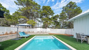 A rectangular swimming pool with a tiled edge, surrounded by artificial green grass. There are two lounge chairs and a table with chairs, and a wooden fence in the background. - Blue Mountain Beach Retreat | Pet-Friendly | Private Pool | 5 Bikes (Santa Rosa Beach)