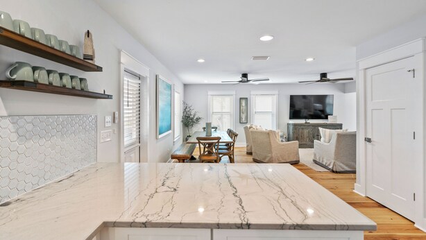 A modern kitchen with a marble countertop, wooden shelves, and a dining area with a table and chairs. - Blue Mountain Beach Retreat | Pet-Friendly | Private Pool | 5 Bikes (Santa Rosa Beach)