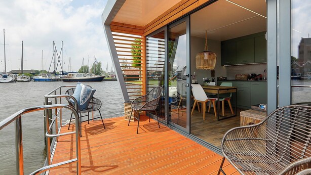 A modern outdoor deck with a wooden floor, metal railings, and wicker chairs.