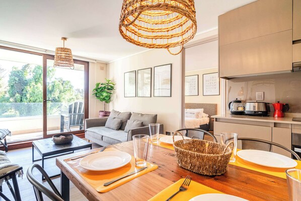 A modern kitchen with a dining area, a sofa, and a view of the outdoors.