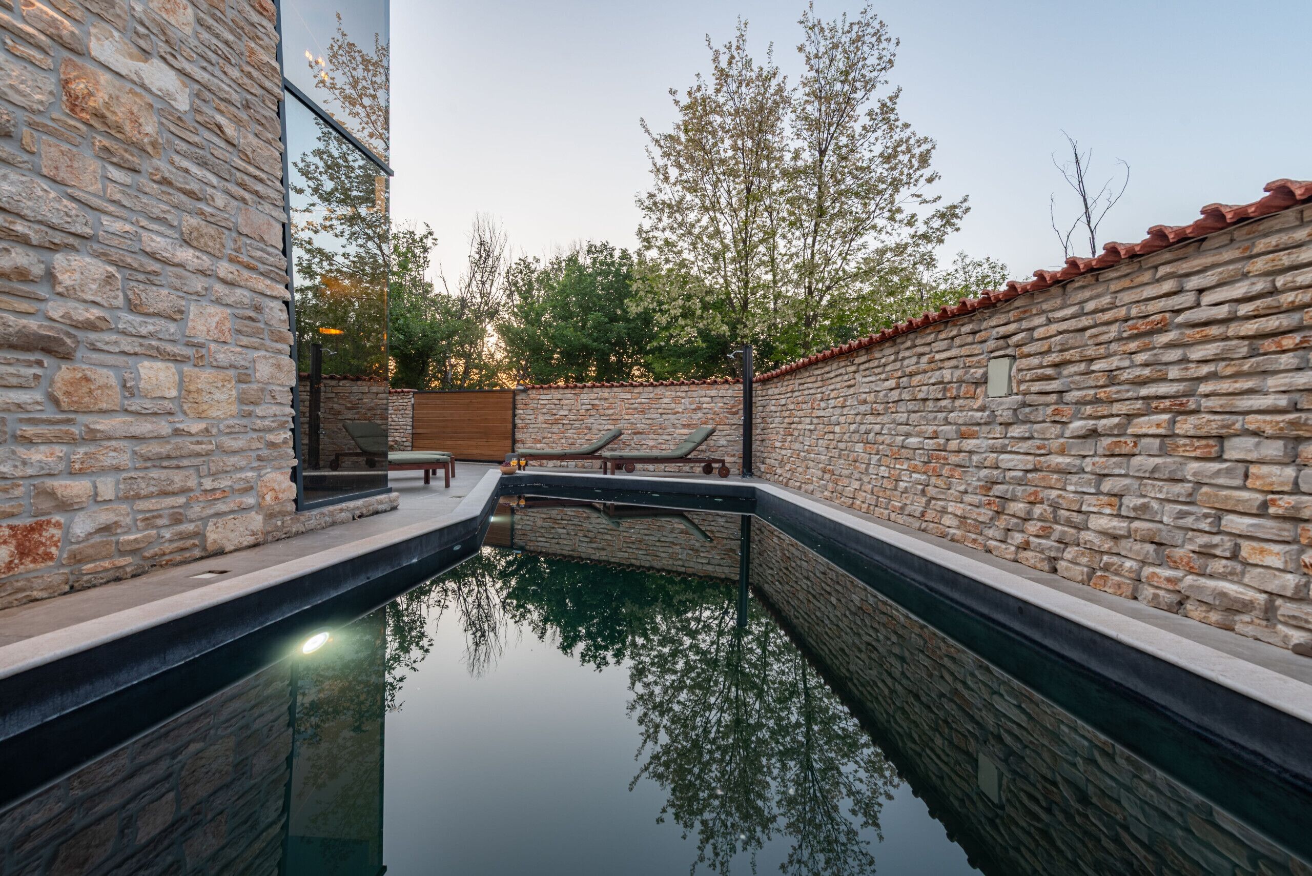 Zona de piscina con paredes de piedra, una cubierta de madera y un banco.