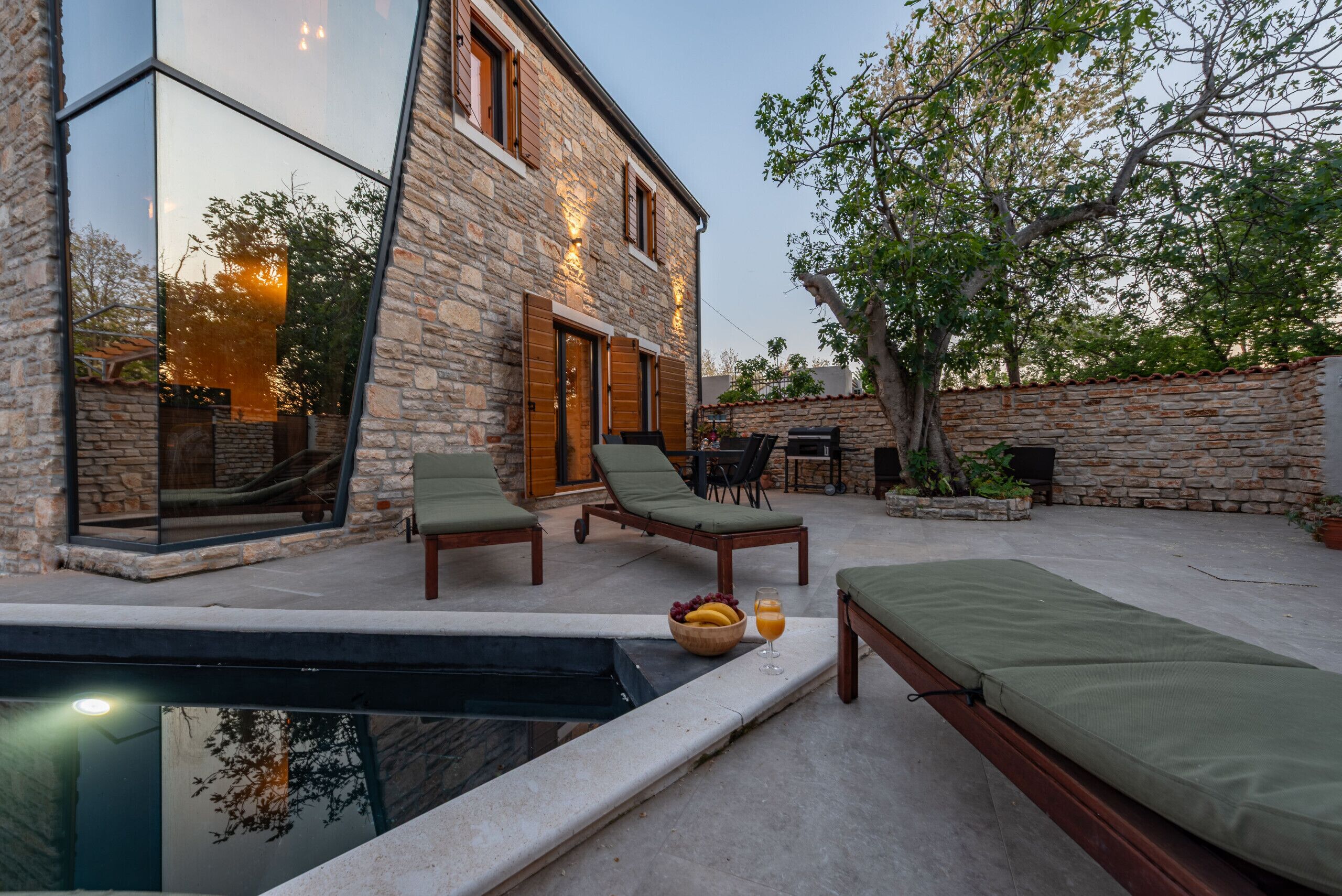 A modern stone building with a swimming pool, lounge chairs, and a dining area.